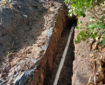 Mini-excavator digging a sewer trench in expansive Texas clay soil, highlighting the equipment costs included in a professional sewer line replacement estimate.